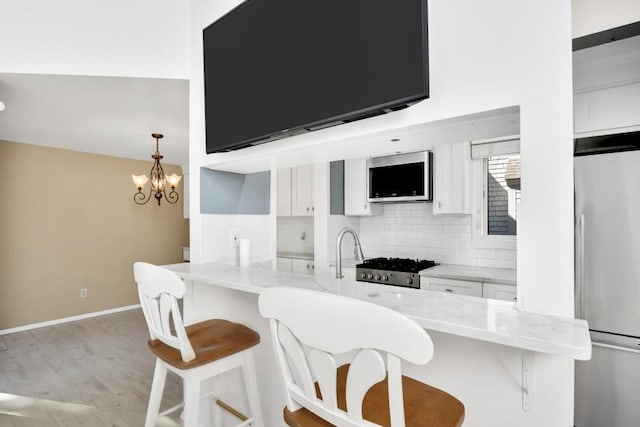 kitchen with a kitchen breakfast bar, appliances with stainless steel finishes, backsplash, white cabinetry, and light stone countertops