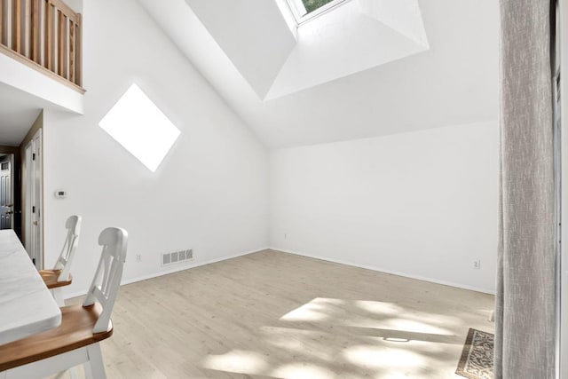 unfurnished office featuring a skylight, high vaulted ceiling, and light hardwood / wood-style flooring