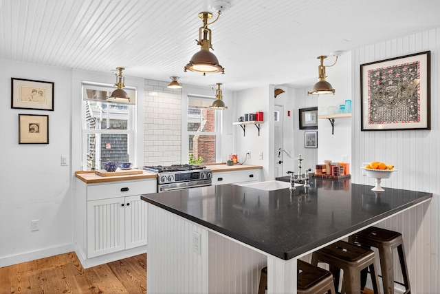 7 Anthony St, Provincetown, MA 02657 - kitchen with stainless steel gas range oven, light wood-style floors, white cabinetry, a breakfast bar, and decorative light fixtures