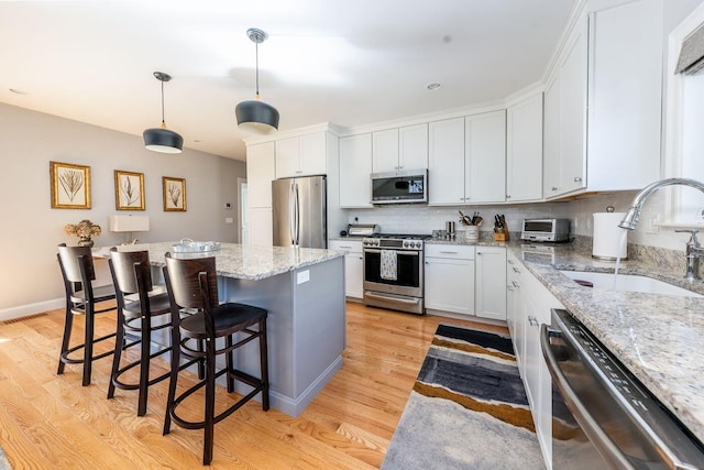 kitchen with stainless steel appliances, a sink, light wood-style floors, a center island, and tasteful backsplash