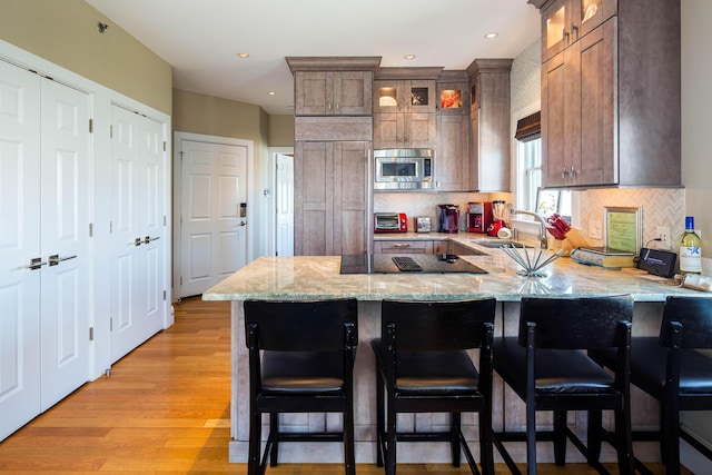 kitchen featuring sink, a kitchen bar, built in appliances, kitchen peninsula, and light wood-type flooring