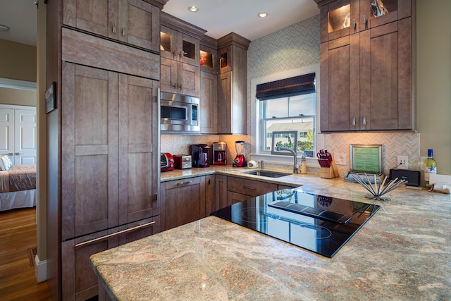 kitchen with sink, light stone counters, tasteful backsplash, built in appliances, and dark brown cabinets