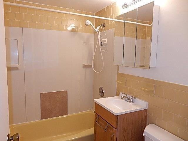 full bathroom featuring tile walls, vanity, tiled shower / bath, and toilet