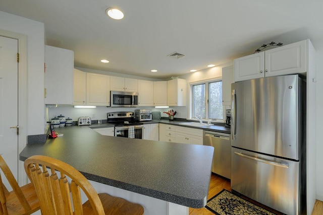 kitchen featuring visible vents, white cabinets, dark countertops, a peninsula, and stainless steel appliances