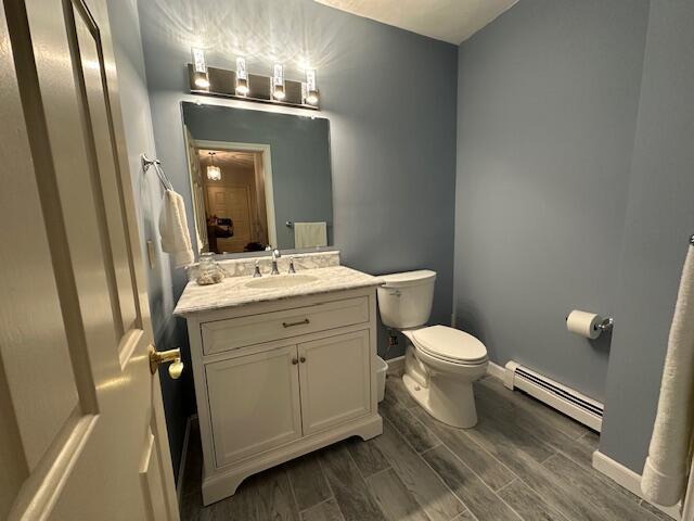 bathroom with toilet, wood finish floors, vanity, baseboards, and baseboard heating