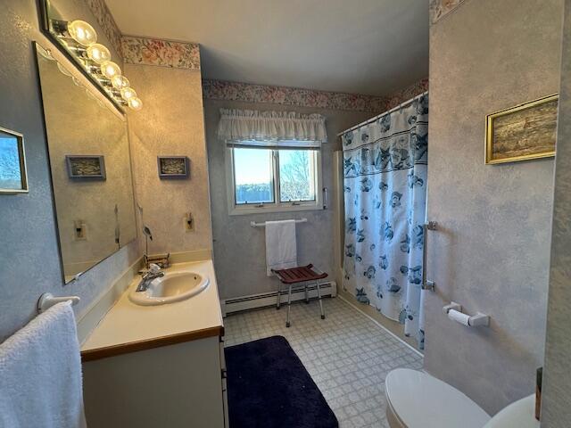 full bathroom featuring curtained shower, toilet, a baseboard heating unit, vanity, and tile patterned floors