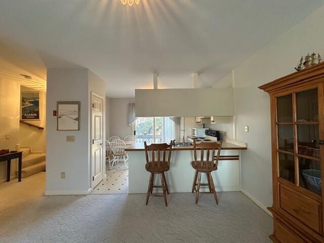 kitchen featuring white microwave, light carpet, a kitchen breakfast bar, a peninsula, and baseboards