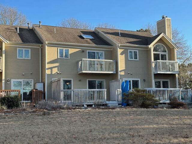 back of house featuring a chimney, a yard, and a balcony