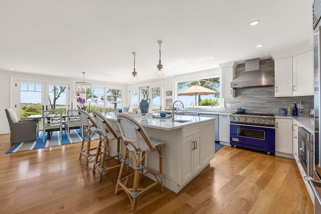 30 Tisquantum Rd, Chatham, MA 02633 - kitchen with wall chimney exhaust hood, designer range, light wood-style floors, white cabinetry, and decorative backsplash