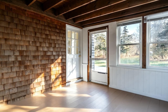 doorway with a wealth of natural light, beamed ceiling, and light wood finished floors