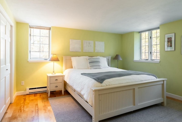 bedroom with baseboard heating, light wood-type flooring, and baseboards