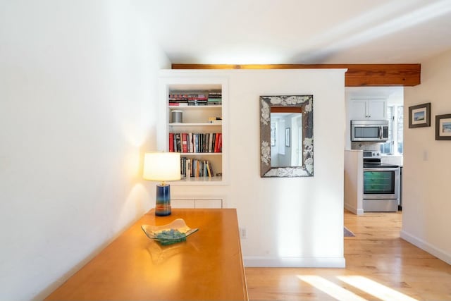 corridor featuring built in shelves, light wood-style flooring, and baseboards
