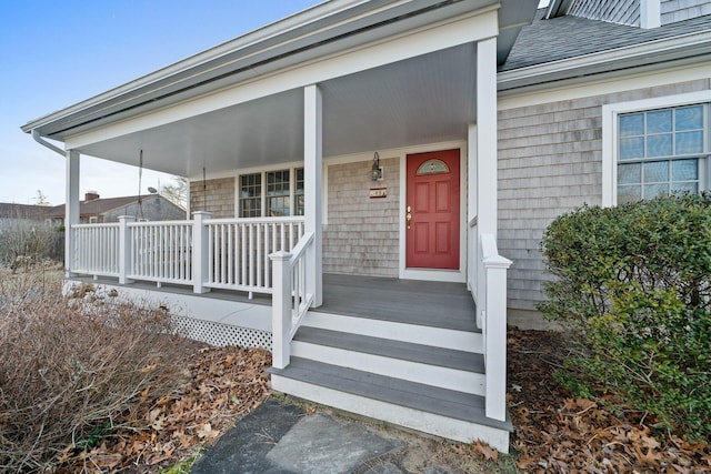 entrance to property with a porch and a shingled roof