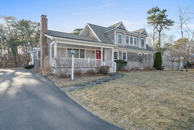 view of front of home with covered porch, a chimney, a front lawn, and a shingled roof