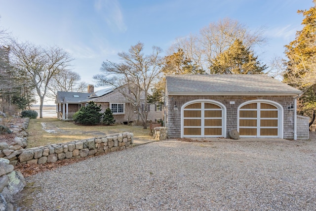 view of front of house with roof mounted solar panels, an outdoor structure, a shingled roof, a garage, and a chimney