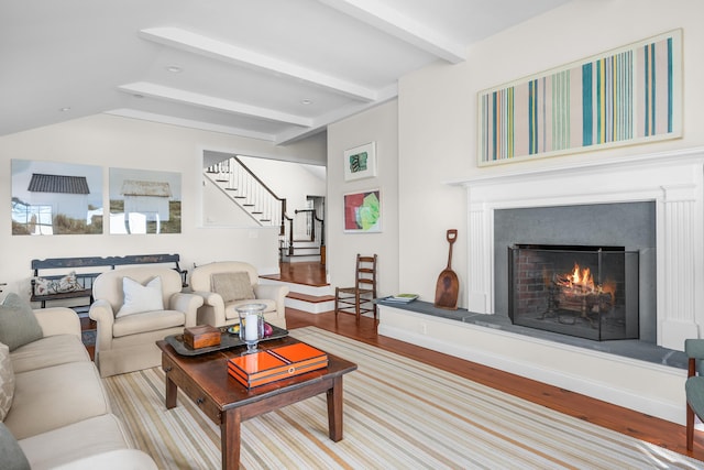 living room with vaulted ceiling with beams, stairs, a lit fireplace, and wood finished floors