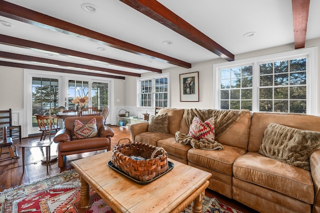 living room featuring beam ceiling, wood finished floors, wainscoting, and a decorative wall