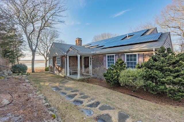 view of front facade with roof mounted solar panels and a chimney