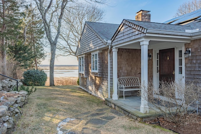 view of side of home featuring a yard, solar panels, a chimney, and a shingled roof