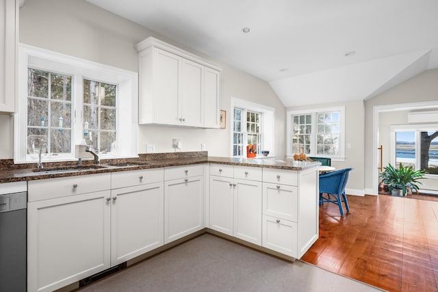 kitchen featuring a sink, stainless steel dishwasher, a peninsula, white cabinets, and lofted ceiling