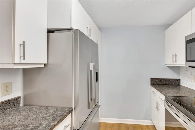 2124 Heatherwood, Yarmouth Port, MA 02675 - kitchen featuring white cabinetry, backsplash, light wood-style floors, stainless steel appliances, and dark stone counters
