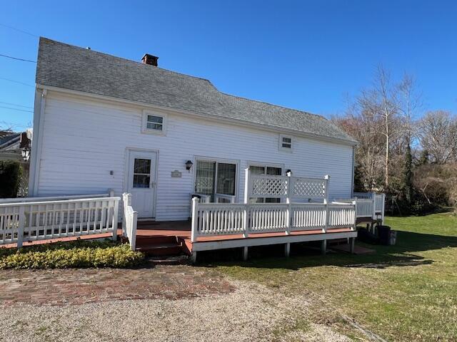 back of house with a wooden deck, a chimney, and a yard