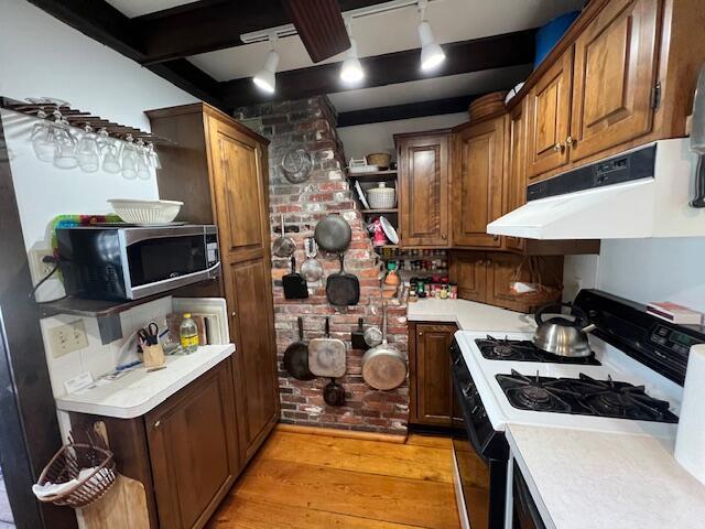 kitchen featuring range with gas cooktop, open shelves, light countertops, stainless steel microwave, and light wood-style flooring
