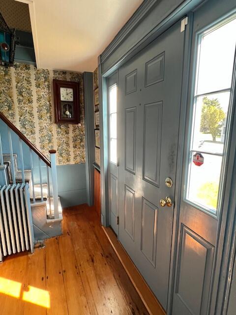 doorway featuring wood-type flooring, wallpapered walls, radiator heating unit, and stairway