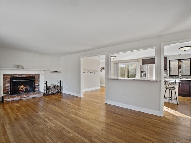 unfurnished living room with a brick fireplace, sink, and hardwood / wood-style floors