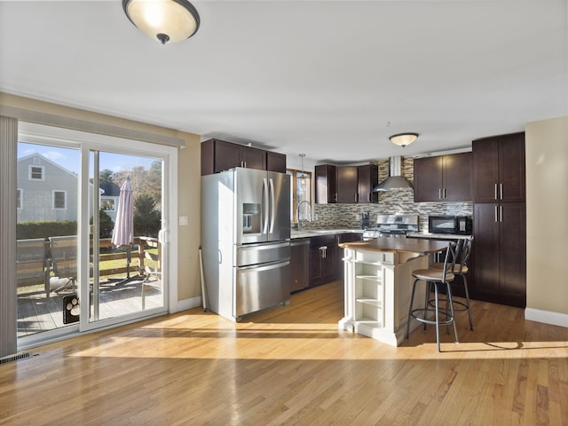 kitchen featuring appliances with stainless steel finishes, a center island, wall chimney exhaust hood, decorative light fixtures, and a kitchen breakfast bar