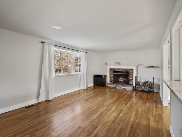 unfurnished living room featuring hardwood / wood-style floors and a brick fireplace