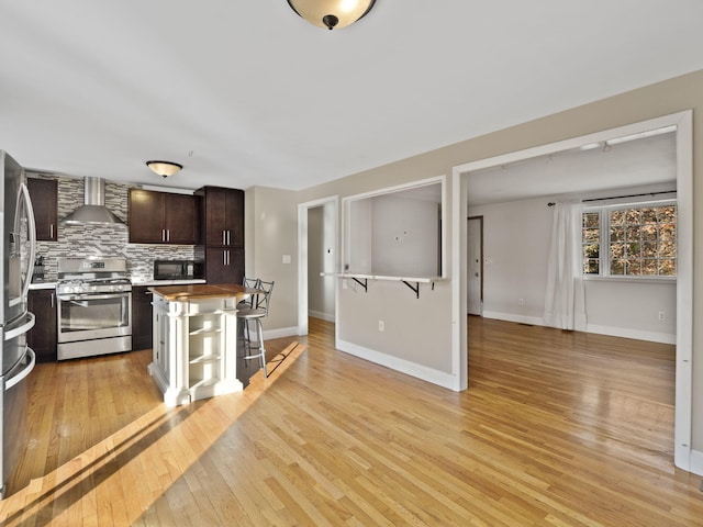 kitchen featuring light hardwood / wood-style flooring, backsplash, a breakfast bar, wall chimney range hood, and stainless steel appliances