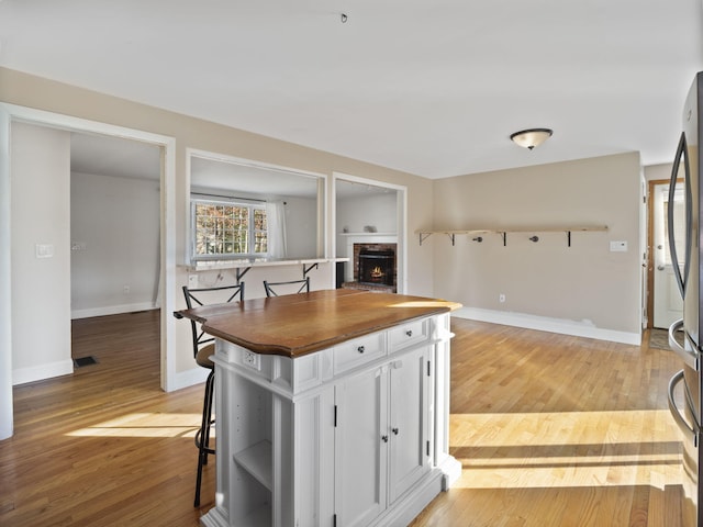 kitchen with a brick fireplace, white cabinetry, stainless steel fridge, and light hardwood / wood-style flooring