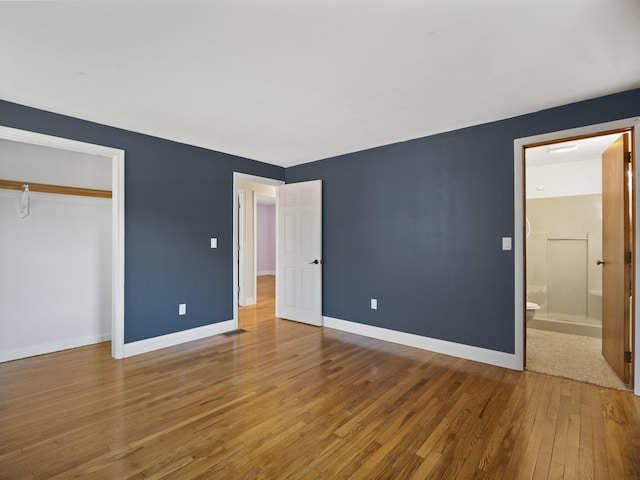 unfurnished bedroom with a closet, ensuite bathroom, and wood-type flooring