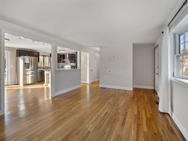 unfurnished living room with light wood-type flooring, track lighting, and sink