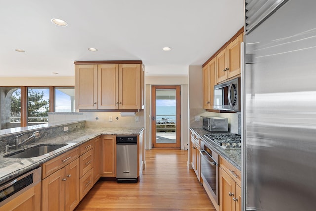 kitchen featuring light stone counters, light wood-style flooring, stainless steel appliances, a sink, and decorative backsplash