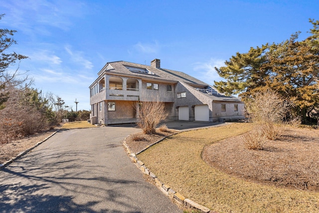 view of front of property with a balcony, a garage, a chimney, and aphalt driveway