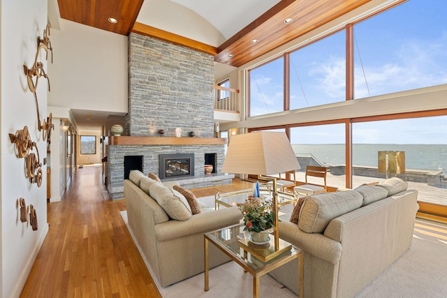 living area featuring baseboards, a water view, a stone fireplace, light wood-style floors, and high vaulted ceiling