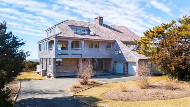 view of front facade featuring driveway, a balcony, and a chimney