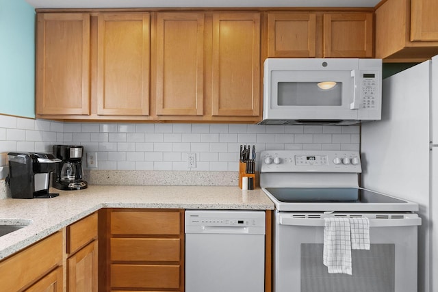 kitchen with white appliances, backsplash, brown cabinetry, and light stone countertops