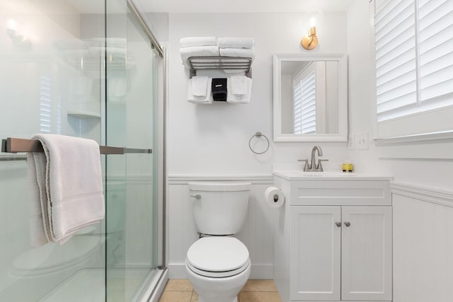 full bath with a wainscoted wall, toilet, a stall shower, tile patterned flooring, and vanity