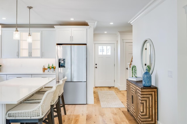 213 N Falmouth Hwy Unit 5B, North Falmouth, MA 02556 - kitchen with stainless steel fridge, white cabinetry, light wood-style flooring, crown molding, and a kitchen bar