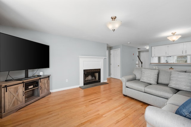 living room with stairway, a fireplace with raised hearth, baseboards, and light wood-style floors