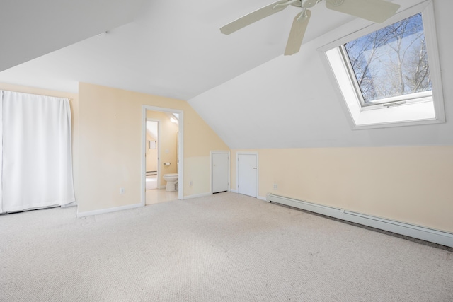 additional living space with a baseboard heating unit, baseboards, carpet flooring, vaulted ceiling with skylight, and a ceiling fan