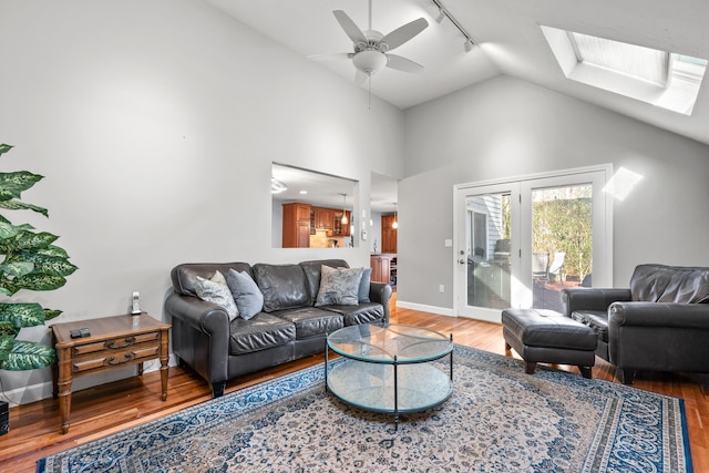 living room with rail lighting, hardwood / wood-style floors, ceiling fan, and lofted ceiling with skylight