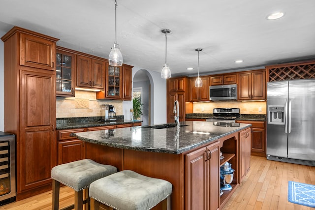 kitchen featuring pendant lighting, appliances with stainless steel finishes, light hardwood / wood-style floors, sink, and a center island with sink