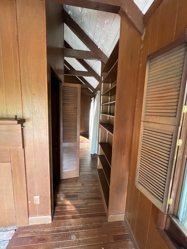 hallway featuring lofted ceiling with beams, wooden walls, and dark hardwood / wood-style floors