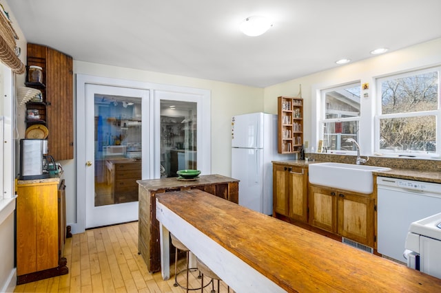 kitchen with visible vents, brown cabinetry, light wood-style floors, a sink, and white appliances