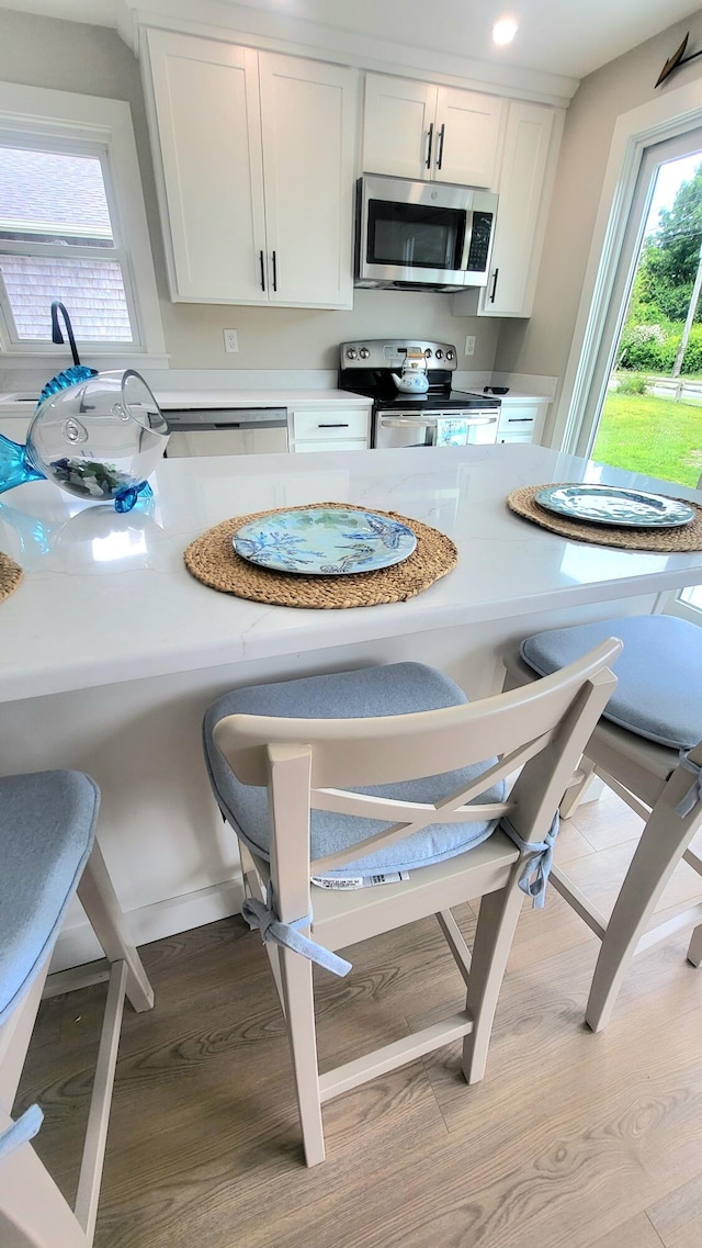 2-A Bodfish Ave, Sandwich, MA 02563 - kitchen featuring appliances with stainless steel finishes, wood finished floors, light countertops, white cabinetry, and a kitchen bar