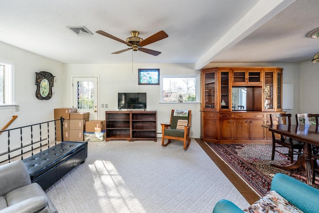 living room featuring beamed ceiling, ceiling fan, a baseboard heating unit, and a textured ceiling